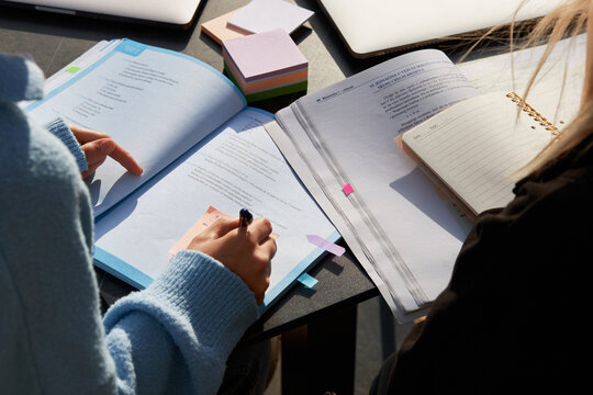 A student's hand writes with a ballpoint pen on note paper in a textbook. Close-up