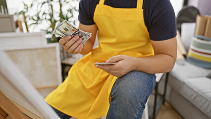 A man in a yellow apron counting dollar bills at a pottery studio
