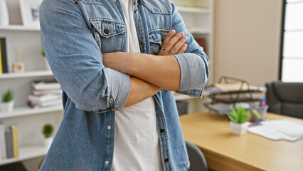 Close-up of a young man with arms crossed wearing denim in a modern office setting.