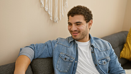 Obraz premium A young man with a beard smiling while relaxing on a sofa indoors at home.