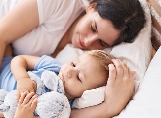 Mother and son sleeping on bed hugging doll at bedroom