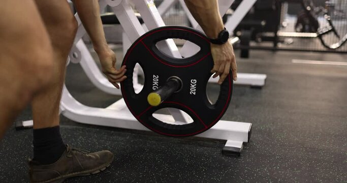 Athlete putting disc for barbell on rack in 20 kg gym closeup 4k movie slow motion. Power load on hands concept