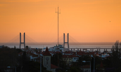 Naklejka premium Vasco da Gama bridge in Lisbon during a beautiful summer sunrise. Orange sky sunrise with landmark Vasco da Gama. Travel to Portugal.