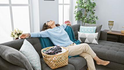 Relaxed middle-aged woman reclining comfortably on a grey sofa in a cozy, well-decorated living...