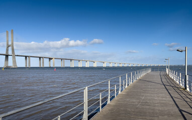 Obraz premium Vasco da Gama Bridge from Lisbon, Portugal, over Tagus river during a beautiful sunny day with blue sky and white clouds. Impressive bride construction.