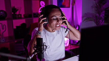 Hispanic woman enjoying gaming in a well-lit room at night, showing excitement and engagement