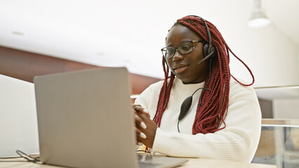 A professional african american woman with braids working in an office wearing a headset and using...