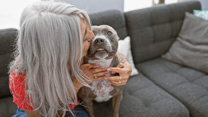 Heartwarming moment, grey-haired middle age woman shares a loving kiss with her dog, sitting...