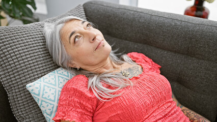 Beautiful middle age woman, with a serious expression innocently settles into her cozy living room...