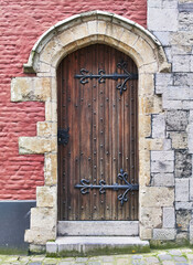 Ancient wooden door with iron hinges on a textured red wall, typical in european medieval architecture.