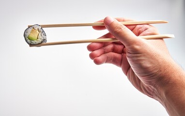 A man expertly grips a sushi roll with chopsticks against a white background, highlighting japanese...