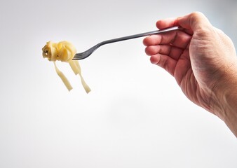 A hand holds a fork twirled with fettuccine pasta against a white background
