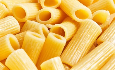 Close-up view of uncooked italian penne pasta with a textured surface and vibrant yellow hue.