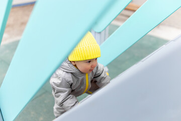 Baby playing on the playground in warm overalls. Outdoor games in cold weather.