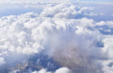 Aerial view of a fluffy cumulus cloudscape with patches of land peeking through, symbolizing travel and nature's grandeur.
