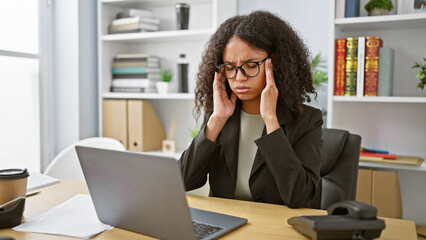 Overworked and stressed, young, beautiful hispanic business woman battles burnout at her office desk, working on laptop