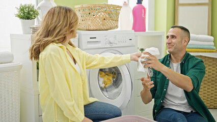 Man and woman couple washing clothes together smiling at laundry room