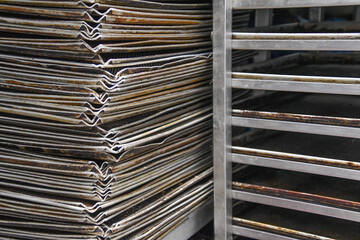 Ein Stapel Backbleche neben einem Stikkenwagen in einer Bäckerei