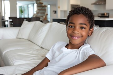 dark-haired boy sitting in a white armchair smiling - obrazy, fototapety, plakaty