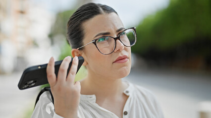 Young beautiful hispanic woman listening to voice message at street