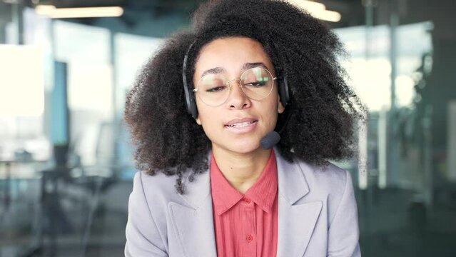 Webcam view. African american female in wireless headset customer service representative operator talking on video call sitting in office. Agent of the call center advises client, answering questions