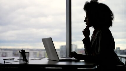 Silhouette. Thoughtful focused young african american female employee working typing on laptop and thinking about problem solving at workplace in office. Serious black woman is busy with a project