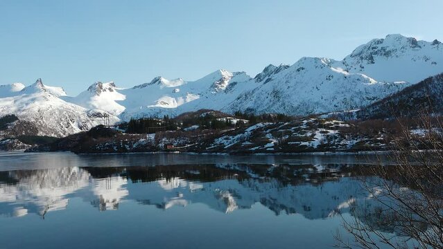 Travel landscape. Nature of Norway. The snowy mountains of the Lofoten Islands. Snow covered mountain range on coastline in winter, View of fjord, reflection in water.