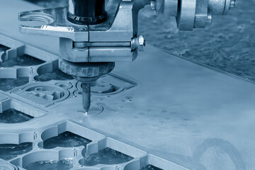 The abrasive waterjet cutting machine cutting the metal plate in the light blue scene.