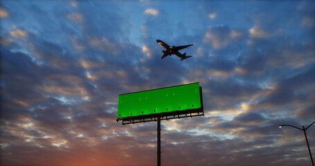 Large airliner with passengers on purple sky is landing at airport of bright sunset on sunny summer day. A cargo plane flies over a billboard with chromakey by the road in the night sky