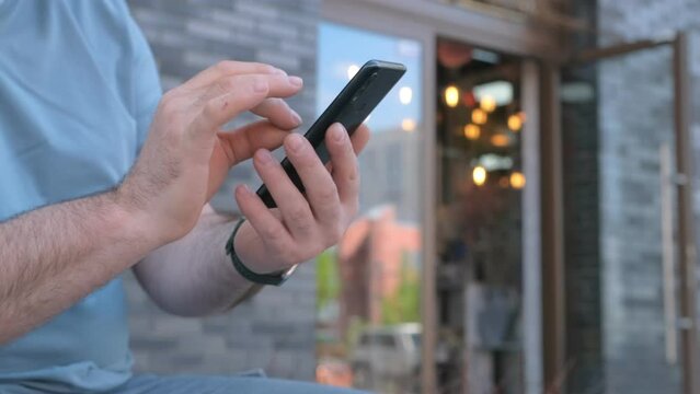 The male on a bench, and scrolls through the pictures in the phone, on promenade of the sea.