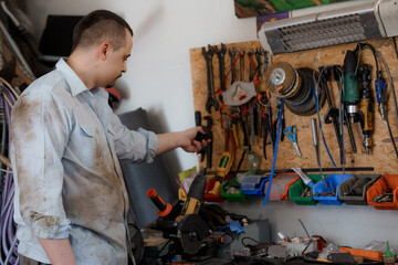 A mechanic stands near a board with tools. Male worker takes a tool