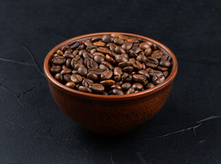 Bowl full of roasted Arabica coffee beans on dark background