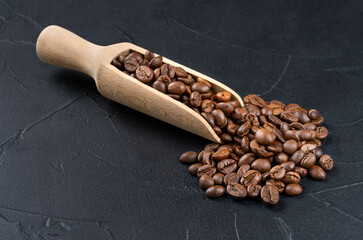 Obraz premium Loose roasted coffee beans from a wooden scoop on a dark background