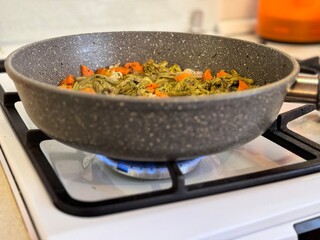 Frying pan on gas stove with roasted bracken with onions and carrots. Healthy eating. Close up.