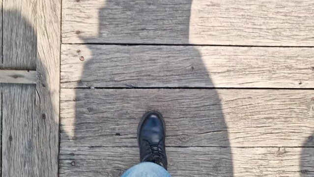 Female legs in blue jeans walk along a wooden bridge, first person view. Close-up of human feet walking on a wooden surface. Tourism and hiking