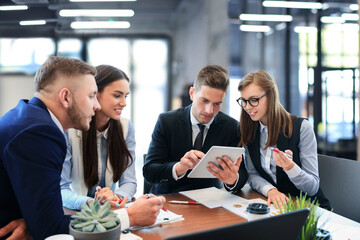 Young handsome man gesturing and discussing something while his coworkers listening to him sitting at the office table