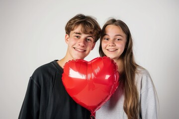 Fototapeta na wymiar a closed mouth smiling teenager couple with a heart shaped balloon on white background