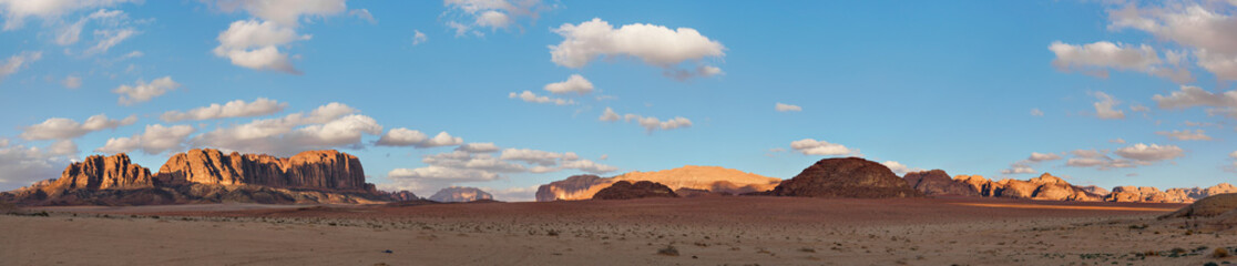 Wide banner panorama of Wadi Rum desert, afternoon sun shines on mountains in distance