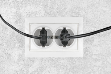 Power electric sockets on a white wall. electric cord plugged into a white electricity rosette on...