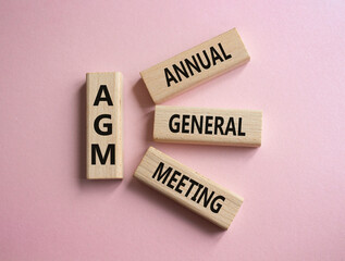 AGM - Annual general meeting symbol. Concept word AGM on wooden blocks. Beautiful pink background....