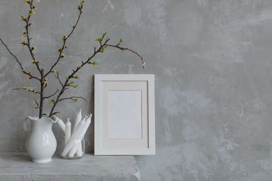 Blank picture frame next to cherry plum branches in a jug and candles on a mantelpiece