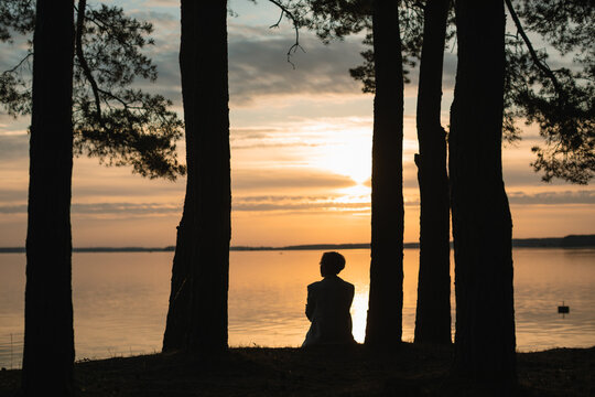 Rear view silhouette of a woman sitting by a lake looking at sunrise, Zaslawskaye Reservoir (Minsk Sea), Belarus