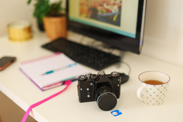  photographer's desk with a camera, a mug of tea, a notepad and a computer