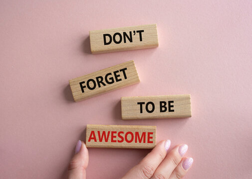 Do not forget to be Awesome symbol. Concept word Do not forget to be Awesome on wooden blocks. Beautiful pink background. Businessman hand. Motivation concept. Copy space