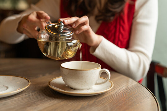 Woman sitting at a table pouring herbal tea into a teacup