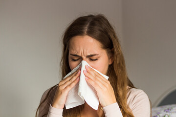 Portrait of woman with allergy blowing her nose. Illness And Sickness. Runny nose. Ill young blond woman having fever and blowing her nose while having a blanket - obrazy, fototapety, plakaty