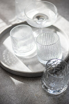 Close-up of assorted wine glasses, champagne coupes, tumblers and glasses on a tray in sunlight