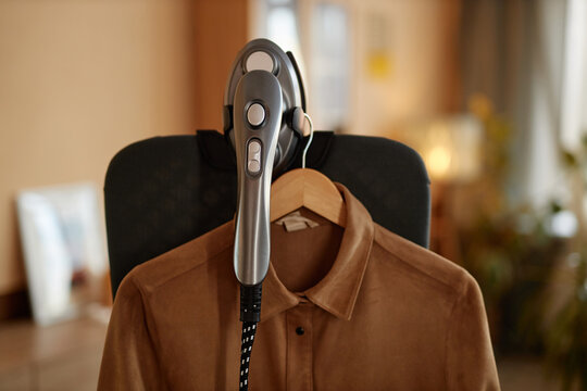 Close up of garment steamer appliance with clothes hanging on vertical ironing board copy space
