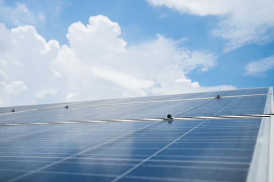 A solar panel on a roof with a clear blue sky in the background. The solar panel is the main focus of the image, and it is surrounded by a few clouds