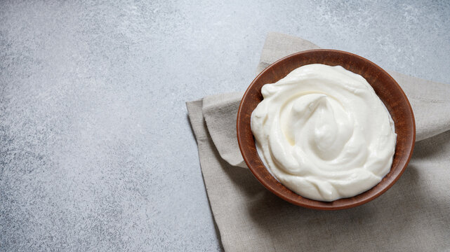 Top view of sour cream or mascarpone cheese in ceramic bowl. Creamy texture. Copy space. Gray concrete background.